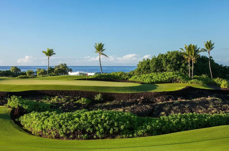 Manicured green framed by lava rock and native planting above the ocean at Kohanaiki