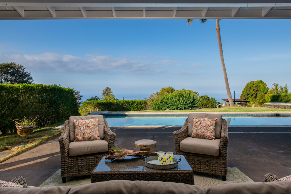 A serene poolside lounge at 76-5876 Hookahi Rd, offering ocean views, cozy outdoor seating, and a peaceful ambiance for ultimate island relaxation.
