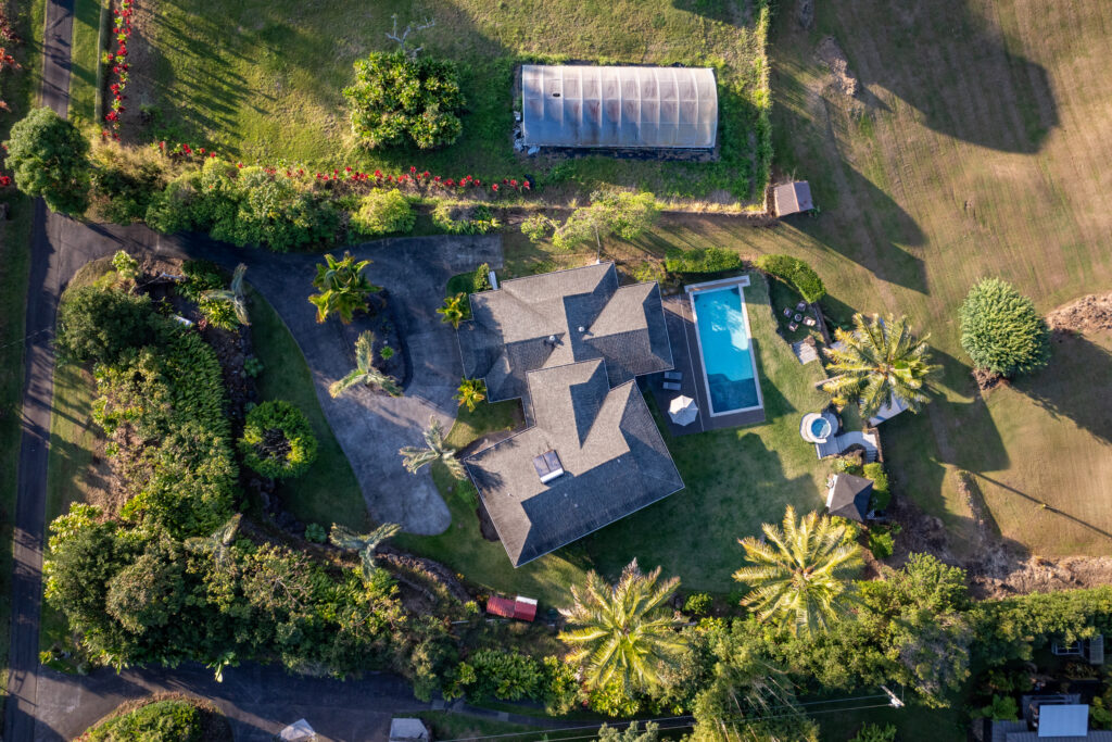 A stunning aerial view of 76-5876 Hookahi Rd, showcasing the luxurious estate, lush tropical landscaping, a private pool, and surrounding greenery in Holualoa, HI.